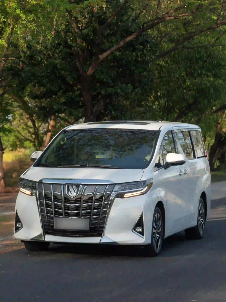White Toyota Alphard VIP transfer vehicle on a tree-lined road