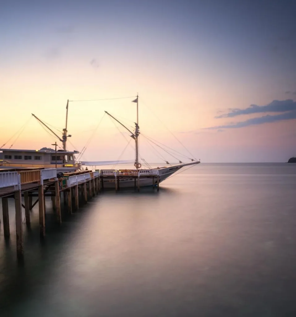 Sailing vessel docked at a wooden jetty at sunset